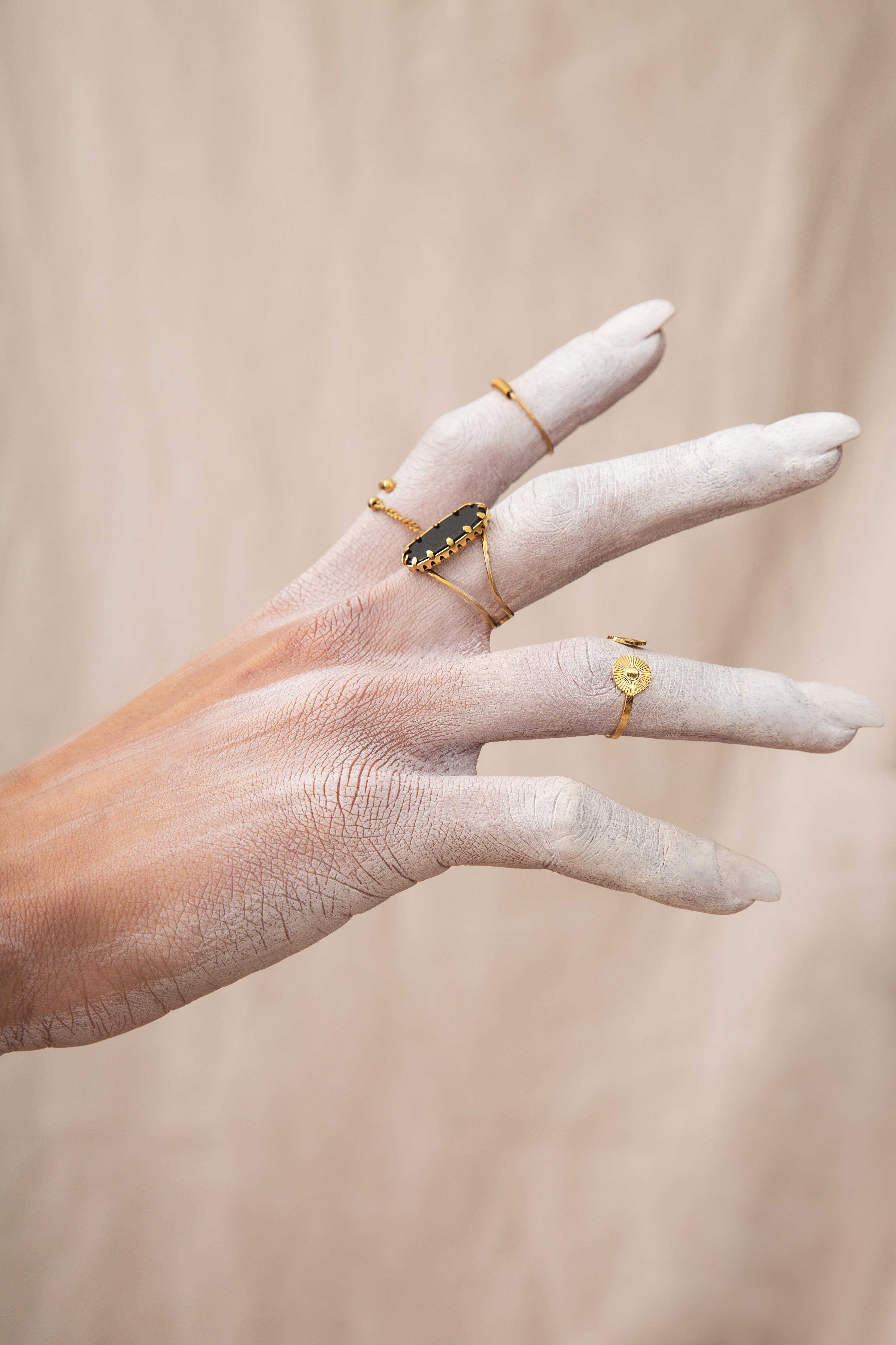 Bague et anneaux dorés portés sur une main blanche poudrée