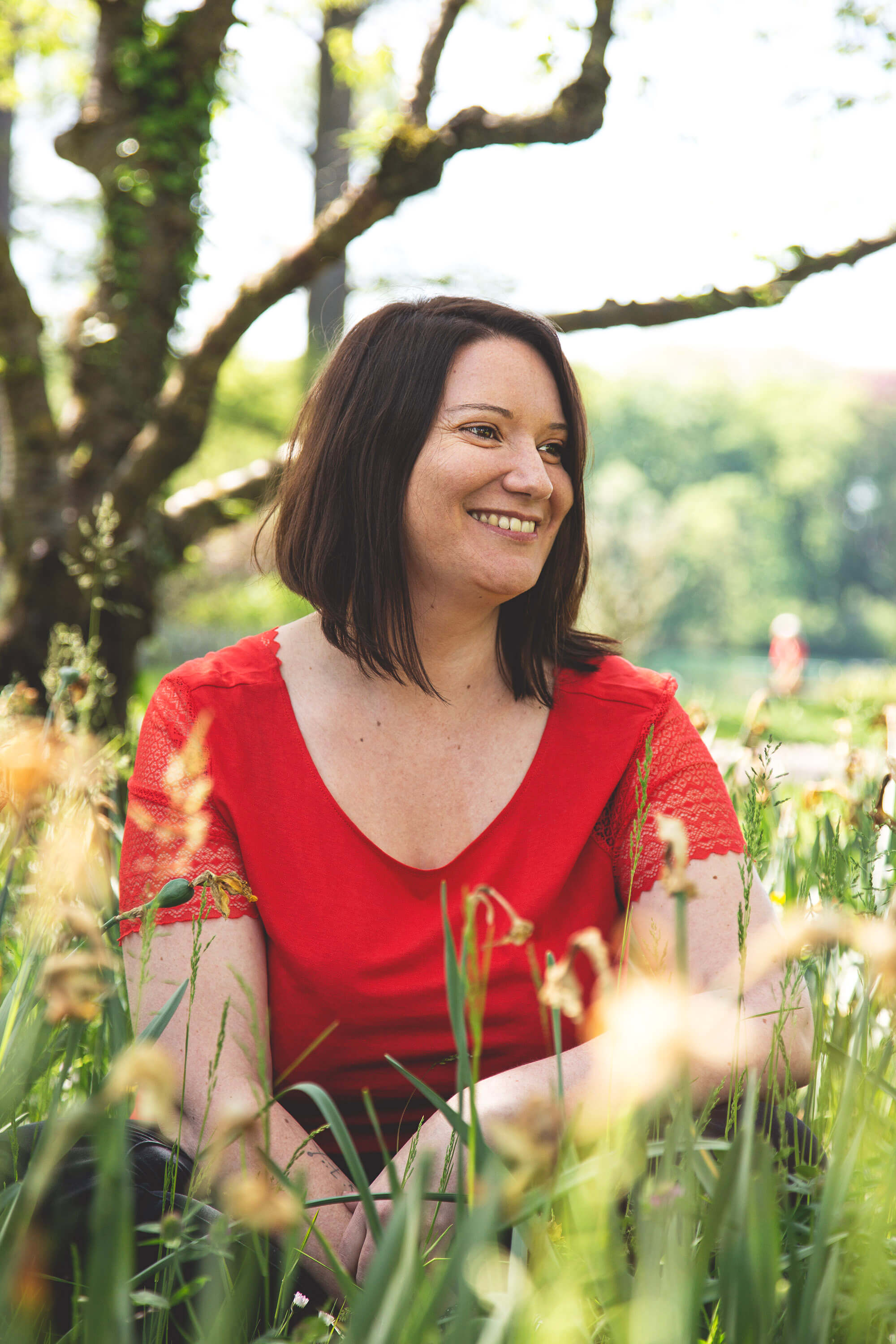 Femme souriante en robe rouge dans un champ, ambiance naturelle et chaleureuse