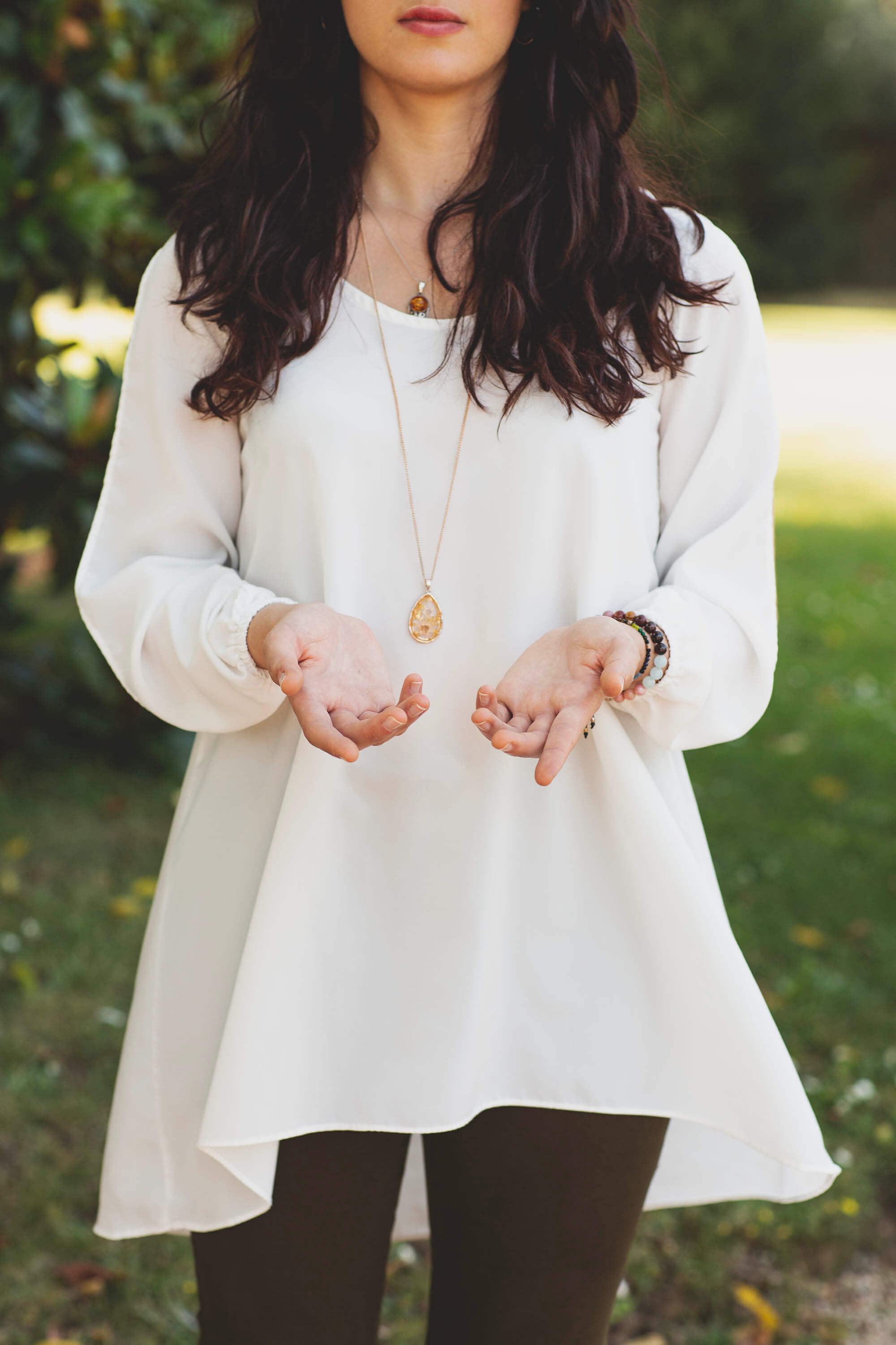 Portrait en extérieur d’une femme en robe blanche tenant les mains ouvertes