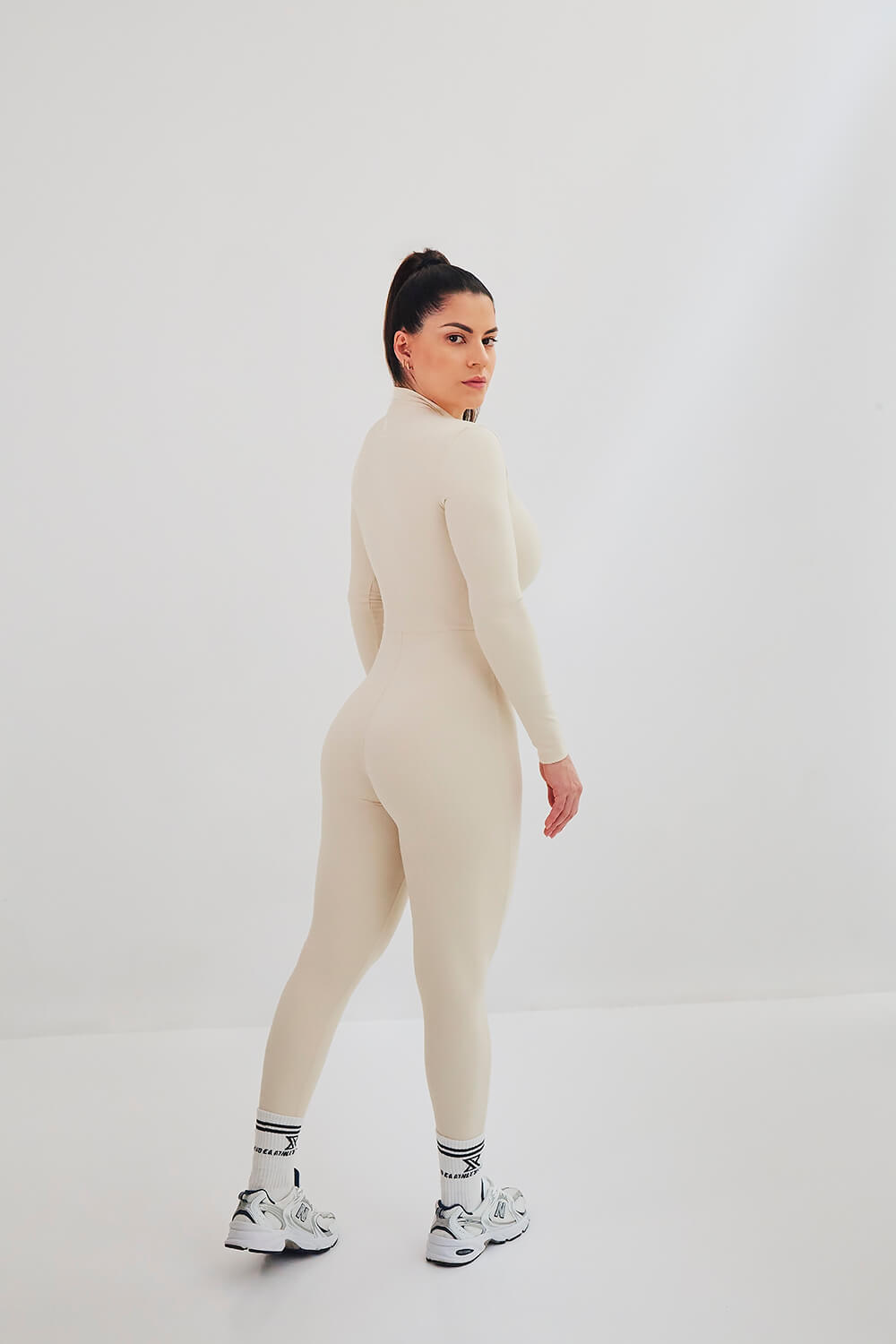 Femme en tenue de sport beige, posant de profil dans un studio de photographie
