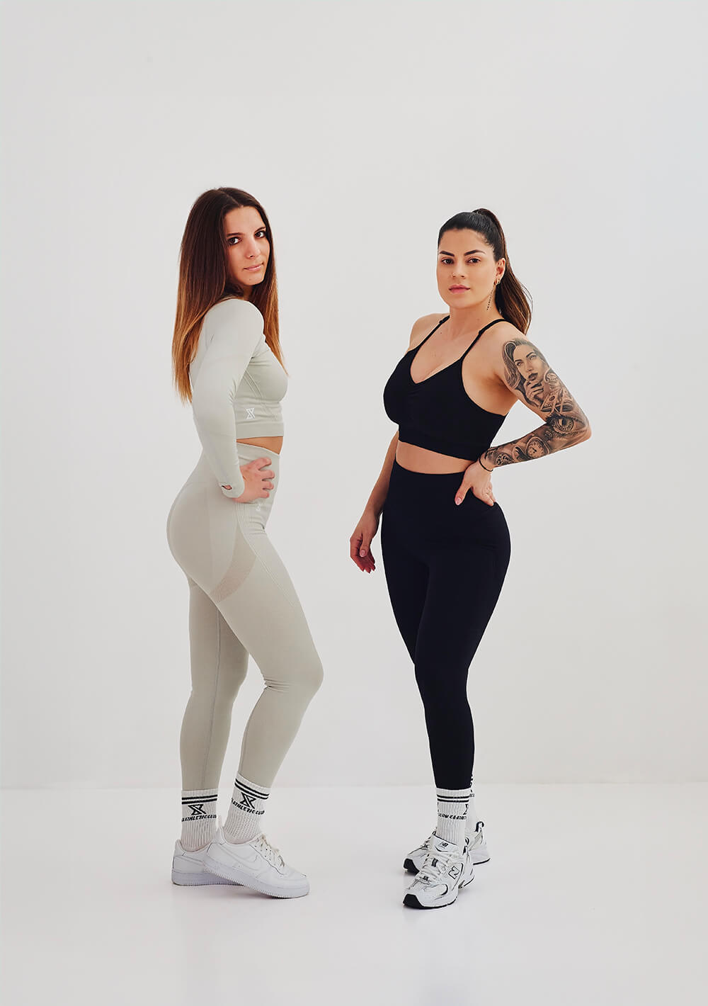 Deux femmes en tenues de sport, l’une en combinaison beige, l’autre en brassière noire et legging noir, posant côte à côte