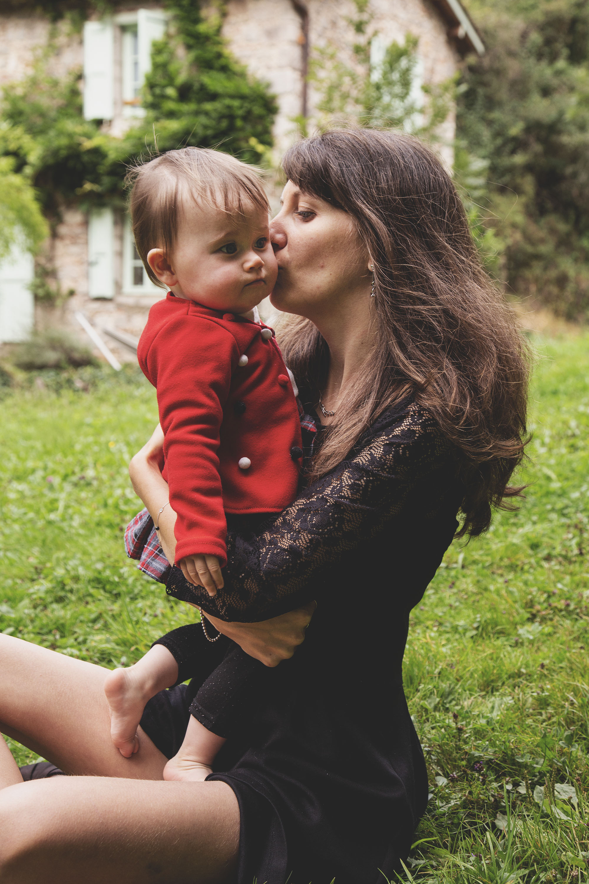 Maman embrassant son enfant en manteau rouge dans un jardin